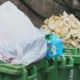 Trash Bags And Organic Waste Overflowing From Green Plastic Bins In An Urban Alleyway